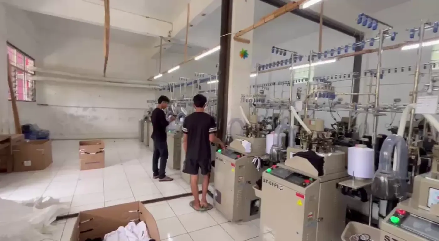 Lantai produksi kaos kaki dengan deretan mesin rajut melingkar yang sedang berjalan