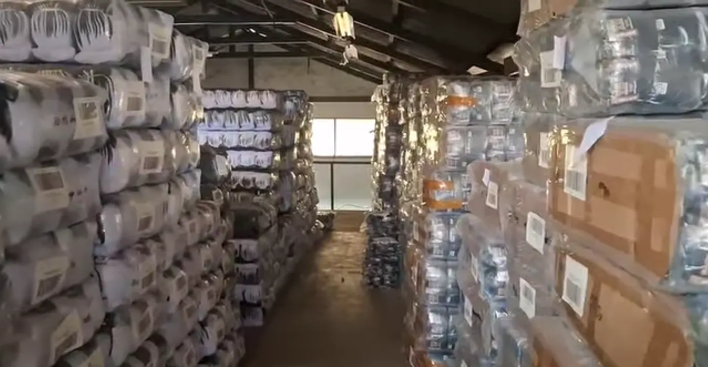 Lorong gudang kaos kaki dengan stok terbungkus dan berlabel tersusun dari lantai sampai atap